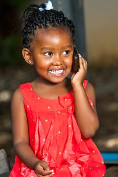 Close up portrait of cute african girl having conversation on smart phone outdoors.