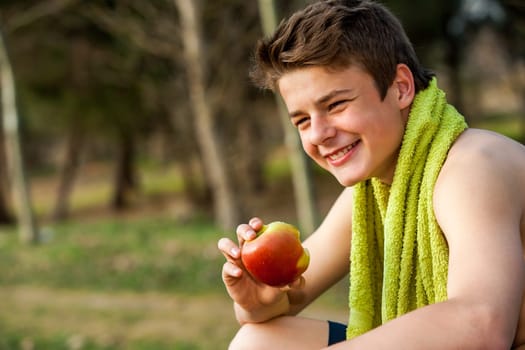 Teen jogger eating apple after exercise outdoors.