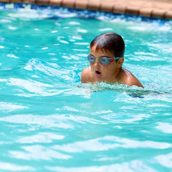 Close up of young boy swimming in outdoor pool.
