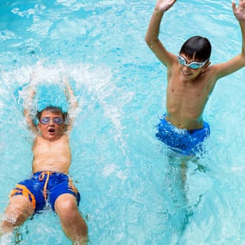 Portrait of two boys splashing water together in pool.