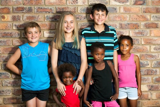 Multiracial group of kids standing together against brick wall outdoors.