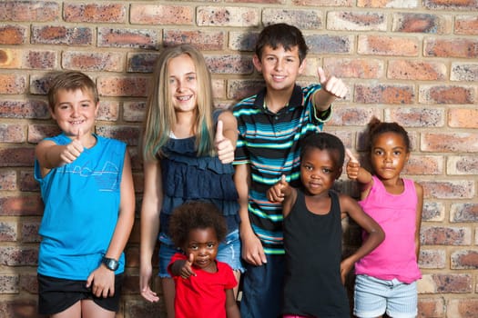 Diversity portrait of kids against brick wall doing thumbs up.