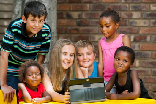 Group of diverse kids playing together on digital tablet outdoors.