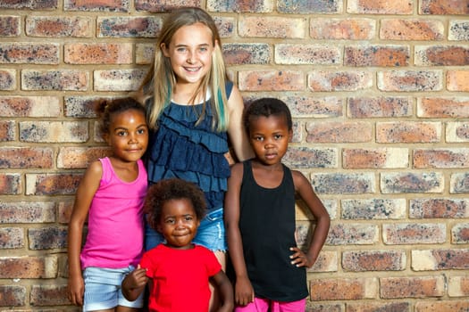 Portrait of cute girl standing with african friends against brick wall.