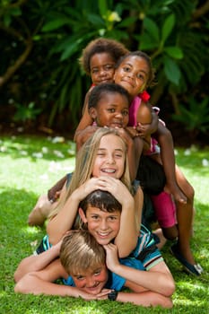 Multiracial children playing together forming human pile in garden.