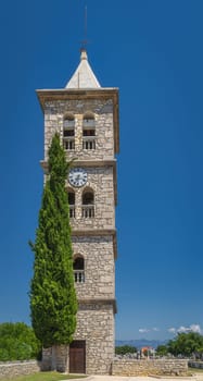 Bell and clock tower of a Church of the Nativity of the Blessed Virgin Mary in Zaton with graveyard and Dinaric Alps in a background, Croatia