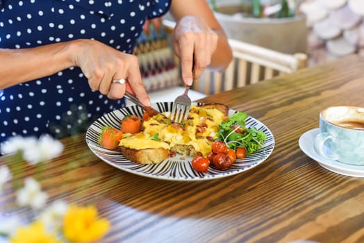 Woman holding knife and fork cutting toast with scrambled eggs pumpkin puree and cubes, smoked salmon and pumpkin seeds