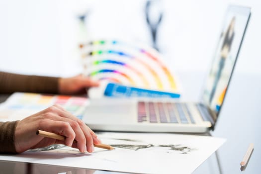 Extreme close up of fashion designers hand making sketch with color chart.