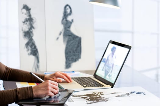 Extreme close up of fashion student designing new collection with digital tablet and laptop.