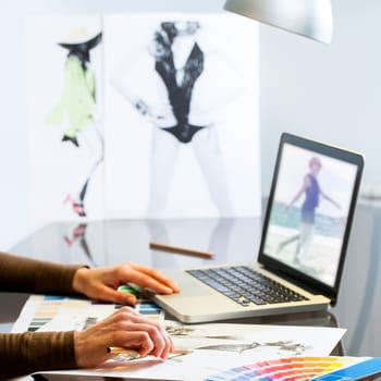 Extreme close up of Fashion Designers hands creating new collection on paper and laptop.