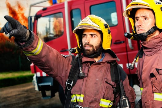 Firemen with fire truck and huge flames in background about to take action.