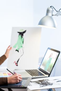 Extreme close up of female hand designing new fashion collection on laptop at table.
