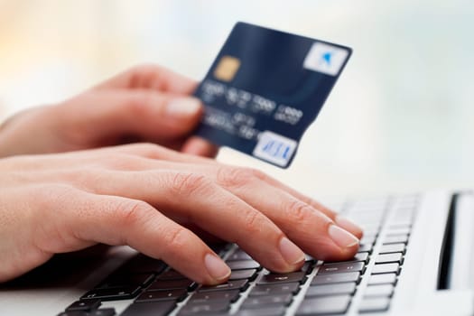 Extreme close up of female hand typing o keyboard with credit card.
