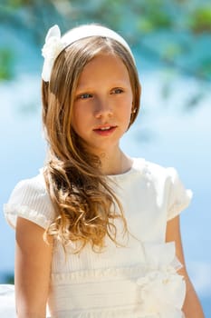Close up portrait of cute girl in white dress and head band outdoors.