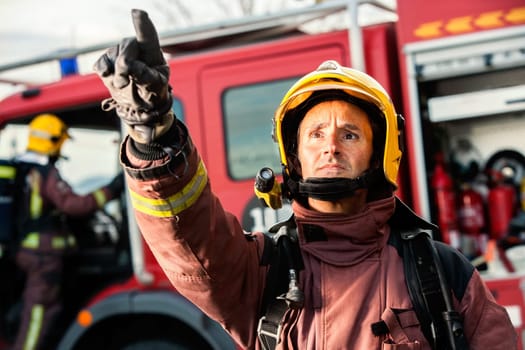 Anxious fireman with fire truck in background pointing at danger situation.