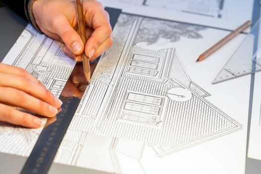 Extreme close up of human hands working on house plan project with pen and ruler.