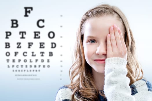Close up portrait of girl reviewing eyesight closing eye with hand.Out of focus test chart in background.