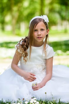 Portrait of cute girl in communion dress holding flowers outdoors.