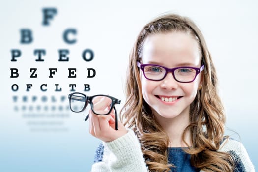 Close up portrait of young girl holding glasses with test chart in background.