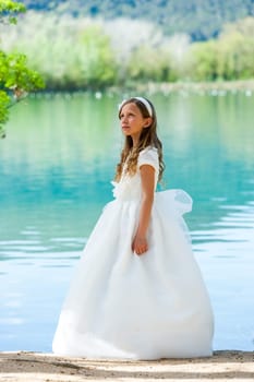 Portrait of cute girl in white dress standing at riverside.