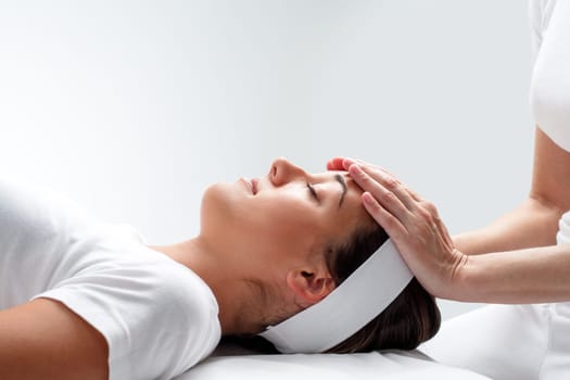 Close up portrait of young woman relaxing at reiki session.Therapist touching girls head with hands.