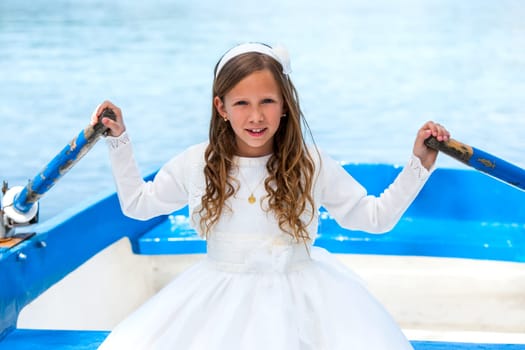 Close up portrait of cute girl in communion dress rowing a boat on river.