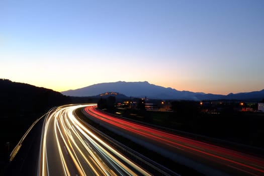 Moving cars leaving rays of colorful lights on busy highway at dusk.