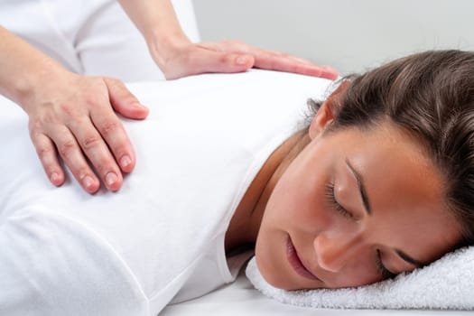 Close up portrait of young woman laying facing head down.Therapist doing reiki treatment with hands on back.