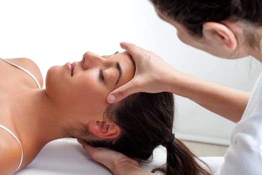 Close up of osteopath doing healing treatment on womans head. Hands doing massage on front and back of head.