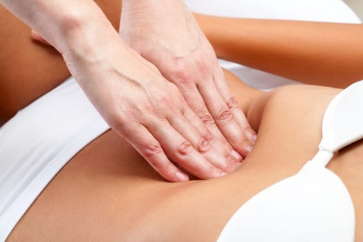 Macro close up of therapist hands doing visceral massage on female abdomen.