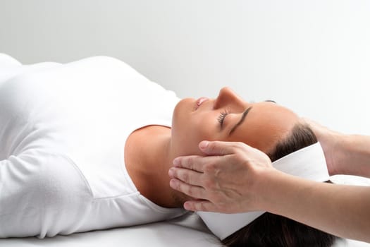 Close up of practitioner doing reiki with hands on young woman. Therapist doing healing treatment with hands next to head.