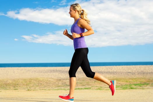 Close up motion portrait of attractive young girl jogging along beach at late afternoon.