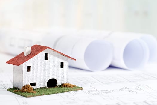 Close up of small toy house on architectural blueprints.