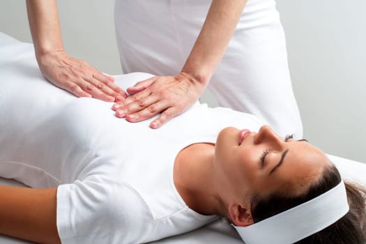 Close up of chiropractor pressing with hands on womans chest at reiki session.