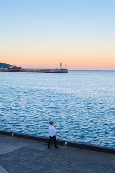 YALTA, CRIMEA, UKRAINE - APRIL 03, 2018: Woman walking by embankment of Yalta at sunset. Lighthouse in the background