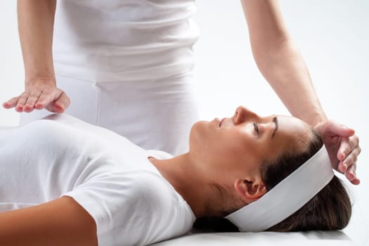 Close up of chiropractor’s hands doing reiki on young woman.One hand on head and one hand on chest.