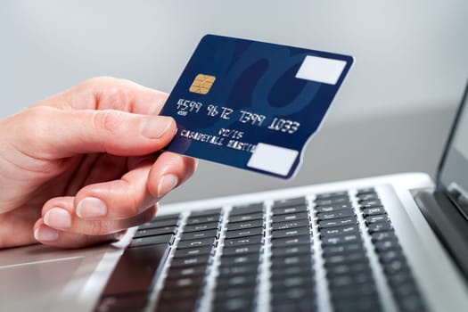Macro close up of female hand holding credit card on laptop.