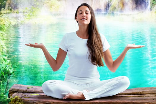 Close up portrait of attractive woman dressed in white sitting in meditating position on wooden log at blue lagoon. Young girl raising hands doing yoga.