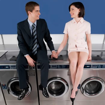Couple holding hands and sitting on washing machines