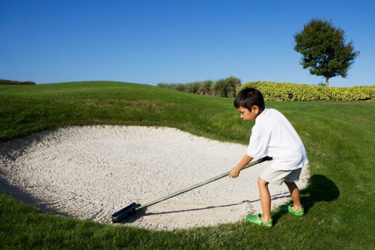 Boy working on a sand trap in a golf course