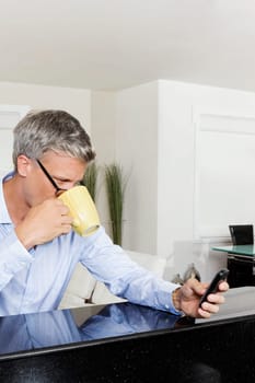 Man drinking coffee and text messaging on a mobile phone
