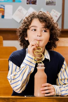 Schoolboy drinking chocolate milkshake in a classroom