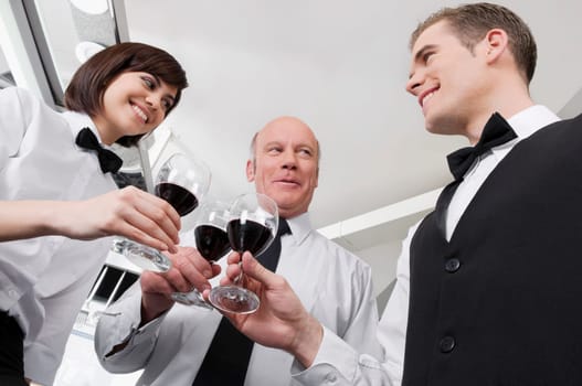 Two waiters and a waitress toasting with wine glasses