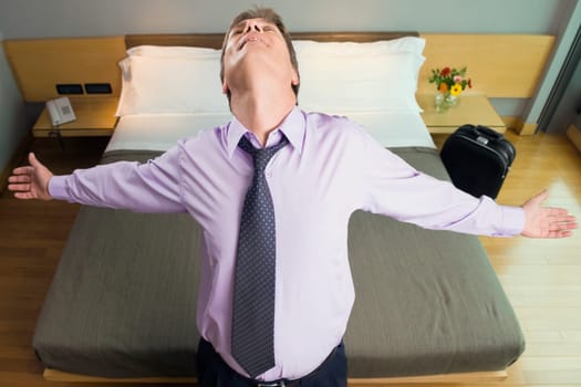 High angle view of a businessman standing with his arms outstretched in hotel room