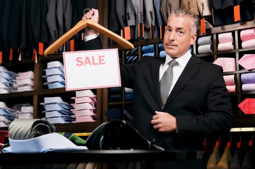 Businessman holding a Sale sign in a clothing store