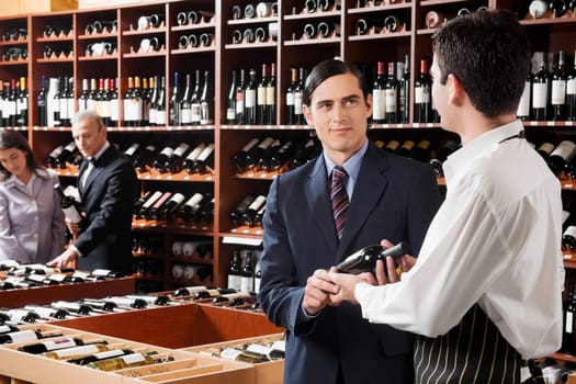 Sales clerk showing a wine bottle to a customer
