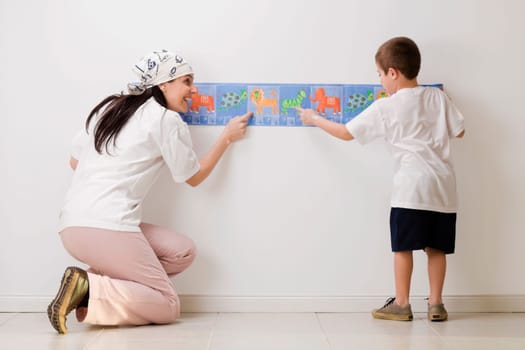Rear view of a boy and his mother pasting wallpaper on the wall