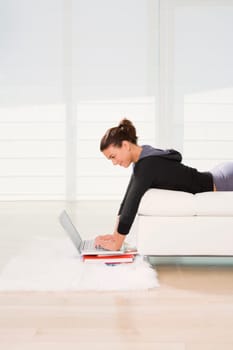 Side profile of a young woman lying on the bed and using a laptop