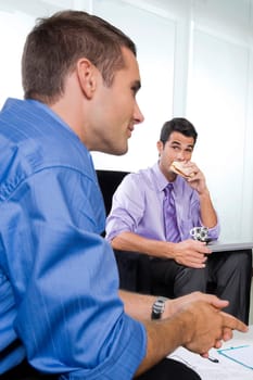 Portrait of a young man eating sandwich and a mid adult man sitting with him