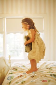 Side profile of a girl playing with a teddy bear on the bed